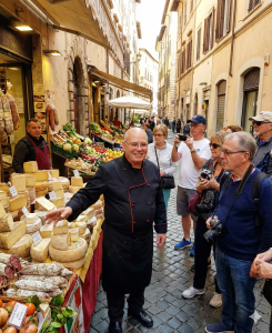 שף שלום שטרית מדריך קבוצת מטיילים בסיור קולינרי באיטליה, מסביר על חומרי גלם טריים בשוק מקומי כחלק מטיול קולינרי חווייתי